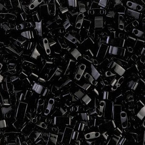 May include: A close-up image of a large quantity of black, shiny, rectangular beads with two holes in each bead.