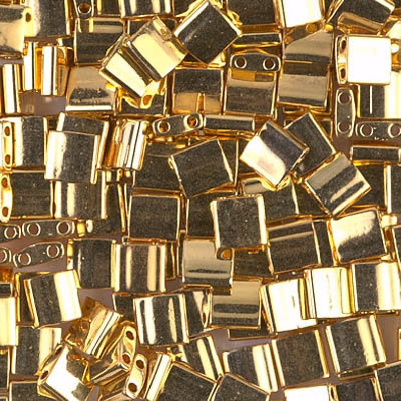 May include: A close-up of a pile of gold-colored metal beads. The beads are square and have a shiny finish.