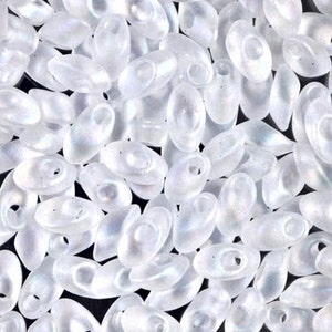 May include: A close-up of a pile of white oval seed beads with an iridescent finish.