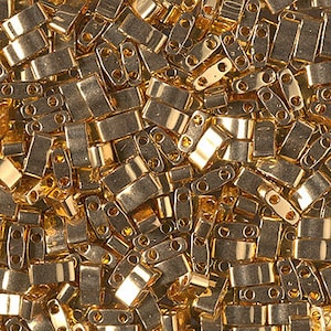 May include: A close-up image of a pile of gold-colored metal beads. The beads are rectangular in shape with two holes on each side.
