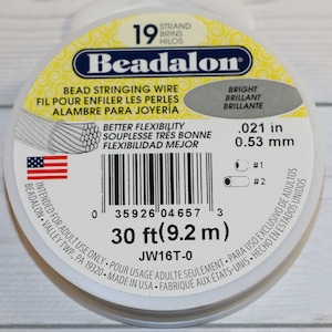 Pode incluir: Uma bobina branca de fio para enfiar contas Beadalon. O rótulo diz "Beadalon" e "Melhor flexibilidade" e lista o tamanho do fio como 0,021 polegadas ou 0,53 milímetros. A bobina contém 30 pés (9,2 metros) de fio.