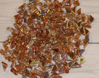 May include: A large pile of iridescent amber glass triangle beads. The beads are small and have a variety of sizes and shapes.