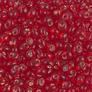 May include: A close-up view of a large quantity of small, red, glass seed beads. The beads are round and have a slightly irregular shape. They have a shiny, translucent finish.