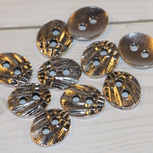 May include: Ten silver-toned buttons with a textured design. The buttons have two holes each and are oval shaped.