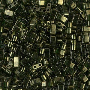 May include: A close-up view of a large quantity of dark green glass seed beads. The beads are rectangular in shape with two holes on each side.