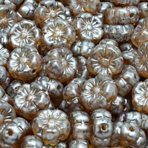 Puede incluir: Primer plano de un montón de cuentas plateadas con forma de flor. Las cuentas tienen un brillo metálico y un agujero para ensartar. Las cuentas están agrupadas, llenando el marco.