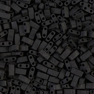 Puede incluir: Vista de cerca de una gran cantidad de cuentas negras de dos agujeros. Las cuentas están hechas de un material mate y tienen una forma ligeramente irregular.