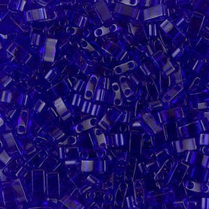May include: A close-up view of a large quantity of small, dark blue, glass seed beads. The beads are all the same size and shape, and they are arranged in a random pattern.