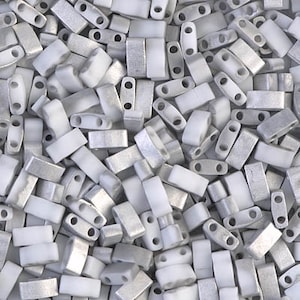 May include: A close-up view of a pile of silver and white rectangular beads. The beads have two holes in each.