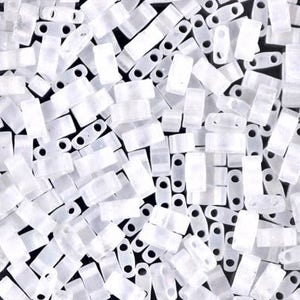 May include: A close-up of a large quantity of small, white, opaque, rectangular beads with two holes. The beads are arranged in a random pattern.