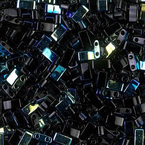 Puede incluir: Una vista de cerca de un montón de cuentas de vidrio negro iridiscente. Las cuentas son de forma rectangular y tienen un acabado brillante y metálico.