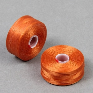 May include: Two spools of orange thread, each wound with a thin, smooth, shiny thread. The spools are made of white plastic.