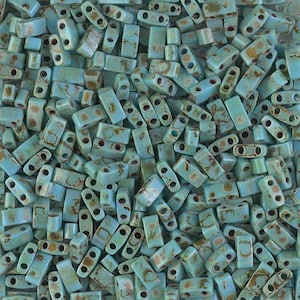 May include: A close-up of a collection of turquoise blue glass beads with gold flecks. The beads are rectangular in shape and have two holes on each side.