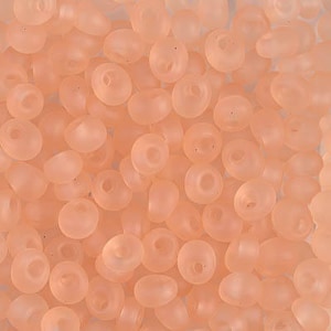 May include: A close-up of a pile of small, round, translucent peach-colored beads. The beads have a slightly irregular shape and a smooth, matte finish.