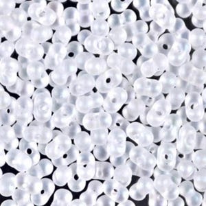 May include: A close-up shot of a pile of translucent white seed beads. The beads are small, oval-shaped, and have a hole running through the center. They are scattered randomly, creating a textured surface. Ideal for jewelry making and crafts.