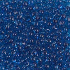 Puede incluir: Una imagen de primer plano de una gran cantidad de pequeñas cuentas azules transparentes. Las cuentas tienen forma de lágrima con un pequeño agujero en la parte superior.