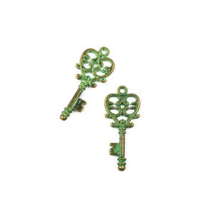 May include: Two antique-style keys with a green and bronze finish. The keys have ornate, heart-shaped tops and detailed stems. The keys are likely used for jewelry making or crafting projects. The keys are on a white background.