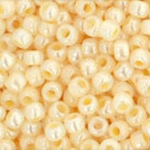 May include: A close-up image of a large quantity of small, round, cream-colored beads. The beads have a slight iridescent sheen.