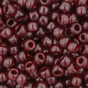 May include: A close-up image of a pile of small, dark red glass beads. The beads are round with a small hole in the center.