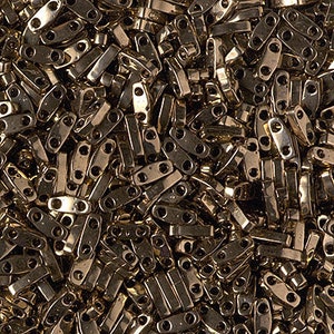 May include: A large quantity of gold-colored metal beads, each bead is shaped like a small, elongated oval with two holes at the top. The beads are arranged in a random pattern, creating a textured surface.