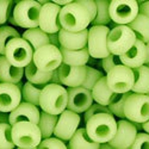 May include: A close-up of a large quantity of small, round, light green beads. The beads are made of plastic and have a smooth, matte finish.