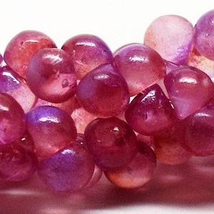May include: A strand of pink and purple iridescent glass beads. The beads are round and have a smooth, polished finish.
