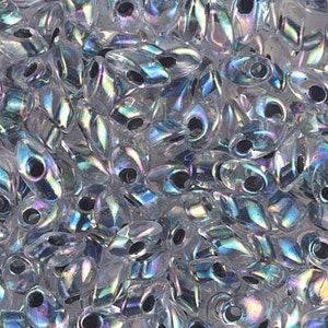 May include: A close-up of iridescent glass seed beads in a teardrop shape. The beads are translucent and have a rainbow sheen.