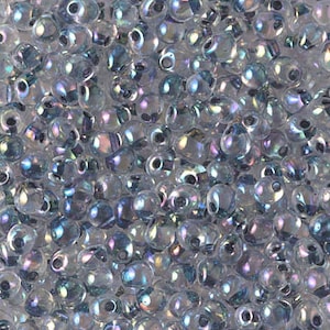 May include: A close-up view of a large quantity of small, iridescent, clear glass seed beads. The beads have a slightly rounded, teardrop shape.