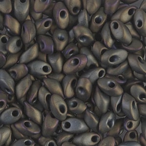 May include: A close-up of a pile of dark brown and iridescent seed beads. The beads are oval shaped with a small hole in the center.