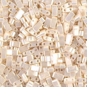 May include: A large pile of small, white, iridescent glass beads. The beads are rectangular with two holes on each side.