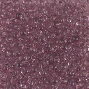May include: A large quantity of small, clear, light purple glass beads. The beads are all the same size and shape, and they are arranged in a random pattern.