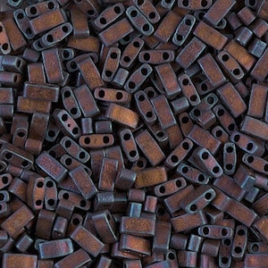 May include: A close-up view of a pile of small, rectangular, iridescent glass beads. The beads are a deep, rich brown color with a hint of blue and green.