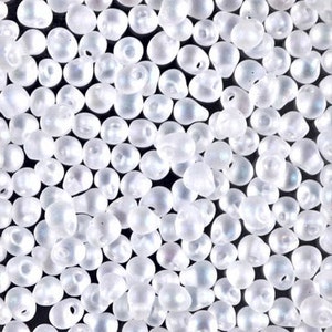 May include: A close-up image of a large quantity of small, white, pearlescent glass beads. The beads are all the same size and shape, and they are arranged in a random pattern.