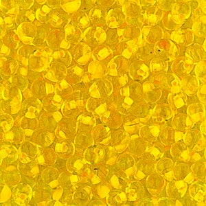 May include: A close-up image of a large quantity of small, round, translucent yellow beads. The beads are arranged in a random pattern and appear to be made of glass or plastic.