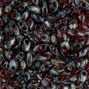 May include: A close-up of a collection of dark red and blue glass beads with white speckles. The beads are oval shaped with a hole in the center.
