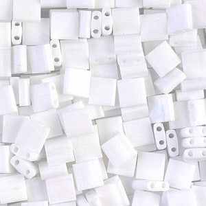 May include: A close-up view of a collection of white square beads with two holes. The beads are made of ceramic and have a smooth, matte finish.