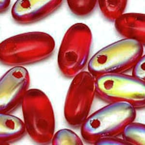May include: Close-up of a collection of red, oval-shaped beads with a hole drilled through each. Some beads have a metallic, iridescent sheen of gold and silver. The beads are scattered on a white surface.