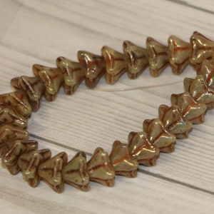 Puede incluir: Hilo de cuentas de cerámica únicas, verde claro y marrón. Cada cuenta tiene forma de flor con superficie texturizada y detalles marrón rojizo. Las cuentas están ensartadas en un cordón transparente, ideal para la creación de joyas.