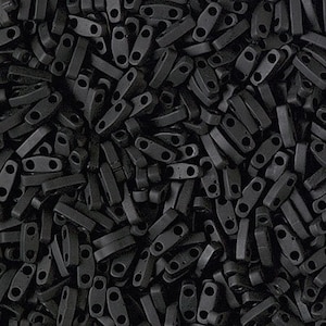 Puede incluir: Vista de cerca de un montón de pequeñas cuentas rectangulares negras mate. Cada cuenta tiene dos agujeros y una forma ligeramente curvada. Las cuentas están dispersas, creando una superficie densa y texturizada.