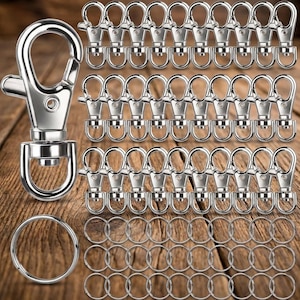 May include: A collection of silver-colored metal swivel lobster claw clasps with spring-loaded gates and attached D-rings, accompanied by a set of circular split key rings. The hardware features a polished finish and a functional rotating swivel base.