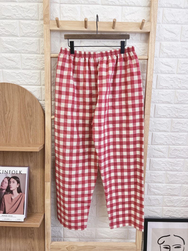 Pu&ograve; includere: Pantaloni a quadri rossi e bianchi appesi a un attaccapanni di legno. I pantaloni hanno un elastico in vita e un design a gamba larga. Il tessuto sembra leggero, adatto all'abbigliamento casual. Il motivo &egrave; un classico quadretto vichy.