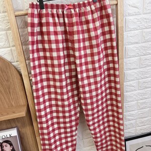 Pu&ograve; includere: Pantaloni da pigiama a quadri rossi e bianchi appesi a un supporto di legno. I pantaloni hanno un elastico in vita con un piccolo fiocco rosa. Il tessuto presenta un classico motivo a quadretti, perfetto per pigiami comodi.