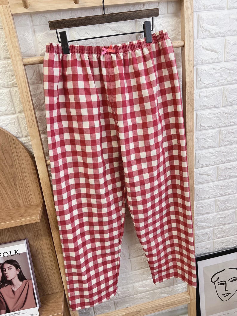 Pu&ograve; includere: Pantaloni da pigiama a quadri rossi e bianchi appesi a un supporto di legno. I pantaloni hanno un elastico in vita con un piccolo fiocco rosa. Il tessuto presenta un classico motivo a quadretti, perfetto per pigiami comodi.
