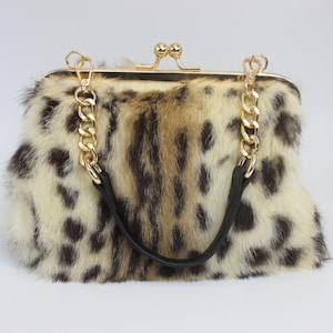 May include: A leopard print handbag with a gold-tone clasp and chain strap. The bag features a black leather handle and a kiss-lock closure. The fur has a cream, brown, and black spotted pattern.