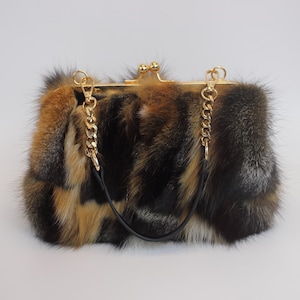 Puede incluir: Un bolso rectangular con un cierre y correas de cadena doradas. El bolso está cubierto con una mezcla de piel marrón, negra y beige. El bolso tiene un asa de cuero negro.