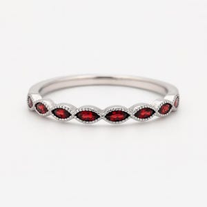 Puede incluir: Un anillo de plata con una fila de piedras preciosas rojas oscuras con corte marquesa. Las piedras están engastadas en una delicada banda con cuentas. El anillo se muestra sobre un fondo blanco, resaltando el brillo de las piedras.