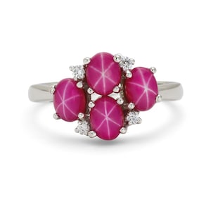 May include: A silver ring featuring five oval, star-shaped, pink gemstones. Small, clear accent stones are clustered around the larger gems. The ring's band is a simple, polished silver.