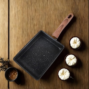 May include: A black rectangular non-stick pan with a wooden handle, alongside three small bowls of food and a cup of sauce, all arranged on a wooden surface. The pan has a speckled interior.