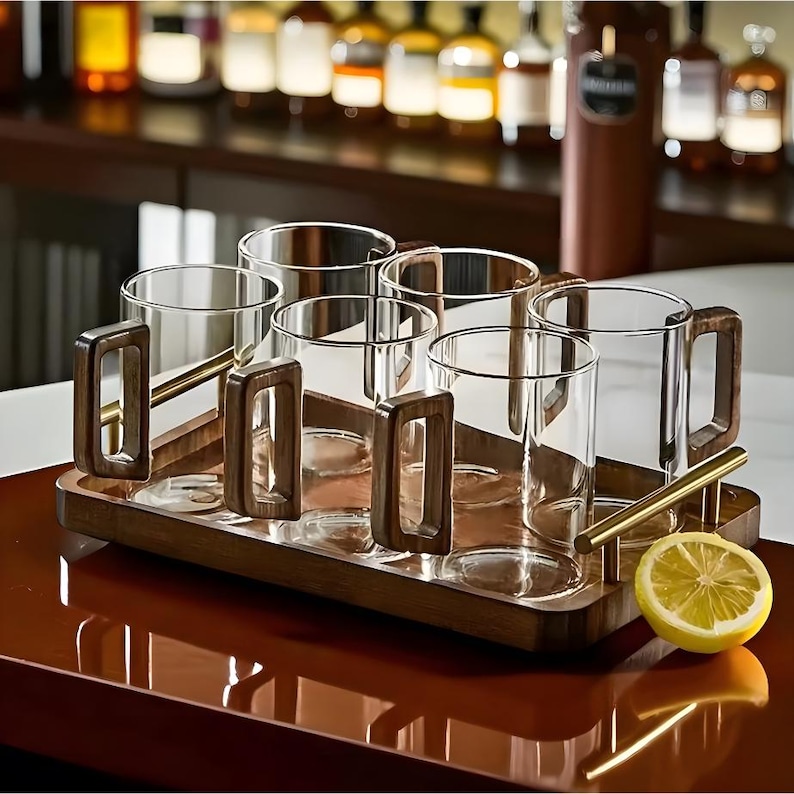 Pode incluir: Um conjunto de seis canecas de vidro transparente com al&ccedil;as de madeira e uma bandeja de servir de madeira. As canecas est&atilde;o dispostas numa bandeja retangular com uma barra de metal dourado. Uma metade de lim&atilde;o est&aacute; na bandeja.