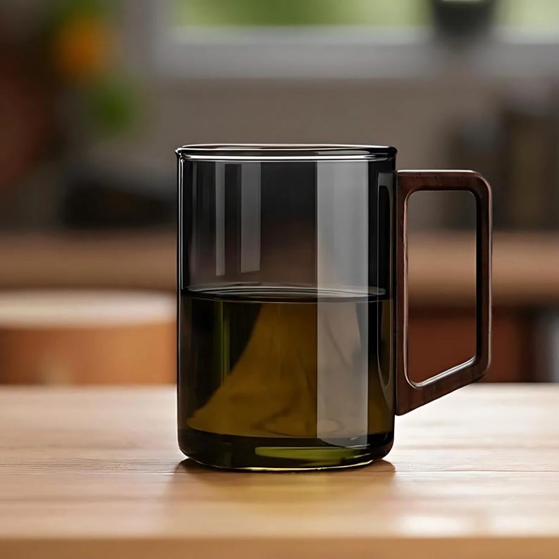 Pode incluir: Uma caneca de vidro transparente com um tom escuro, cheia de l&iacute;quido. A caneca tem uma al&ccedil;a retangular de madeira. A caneca est&aacute; sobre uma superf&iacute;cie de madeira.